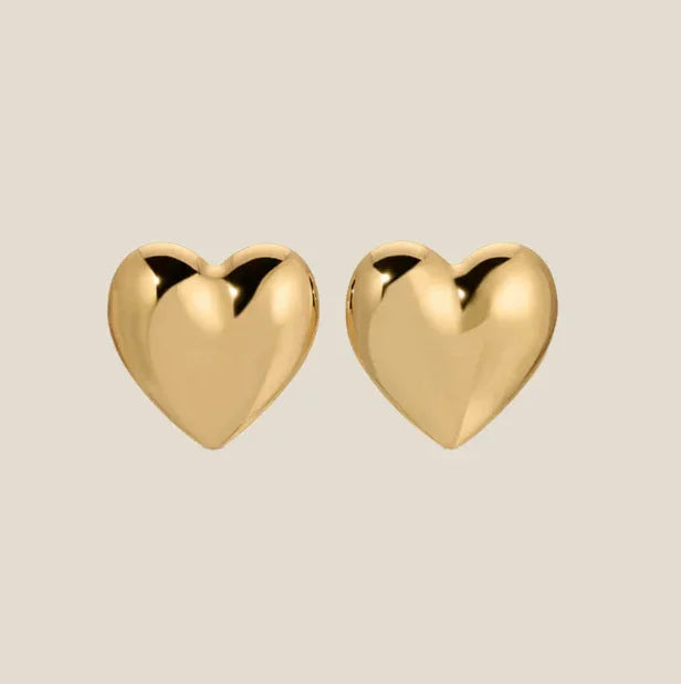 Gold heart stud earrings on beige background from Olivia The Label